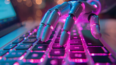 Metallic robotic hand on glowing keyboard with pink and blue neon lights.